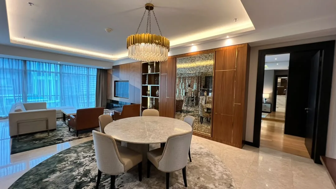 The Ritz-Carlton Residences Kuala Lumpur — dining area with round marble table and brass chandelier, opening to the living room and a corridor beyond