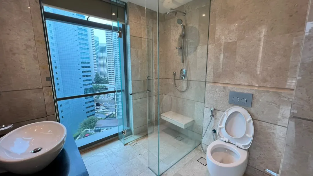 The Ritz-Carlton Residences Kuala Lumpur — marble bathroom with walk-in rain shower, bench seat and a full-height window over the KLCC skyline