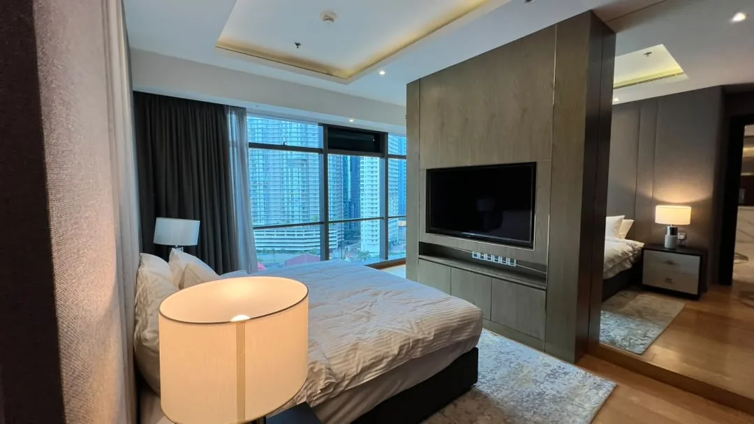 The Ritz-Carlton Residences Kuala Lumpur — bedroom with city view, timber feature wall with wall-mounted television and a mirrored dressing area