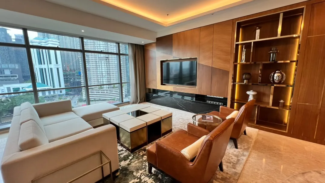 The Ritz-Carlton Residences Kuala Lumpur — living room with corner windows, marble-backed television wall and a lit timber display shelf
